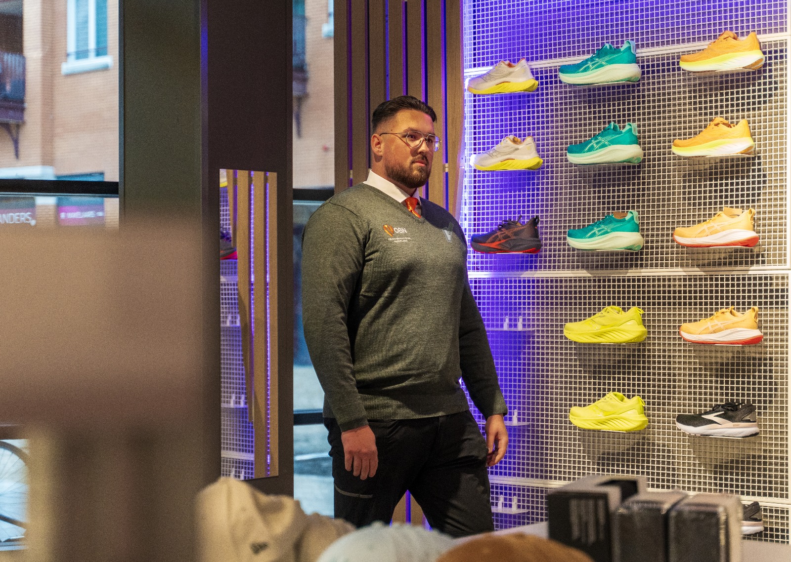 OBN-beveiliger bij een wand met sportschoenen in een winkel
